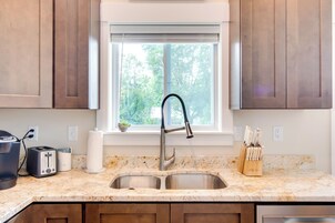 Una cocina con un lavamanos doble, una ventana sobre el lavamanos y una encimera con cafetera, tostadora y bloque de cuchillos.