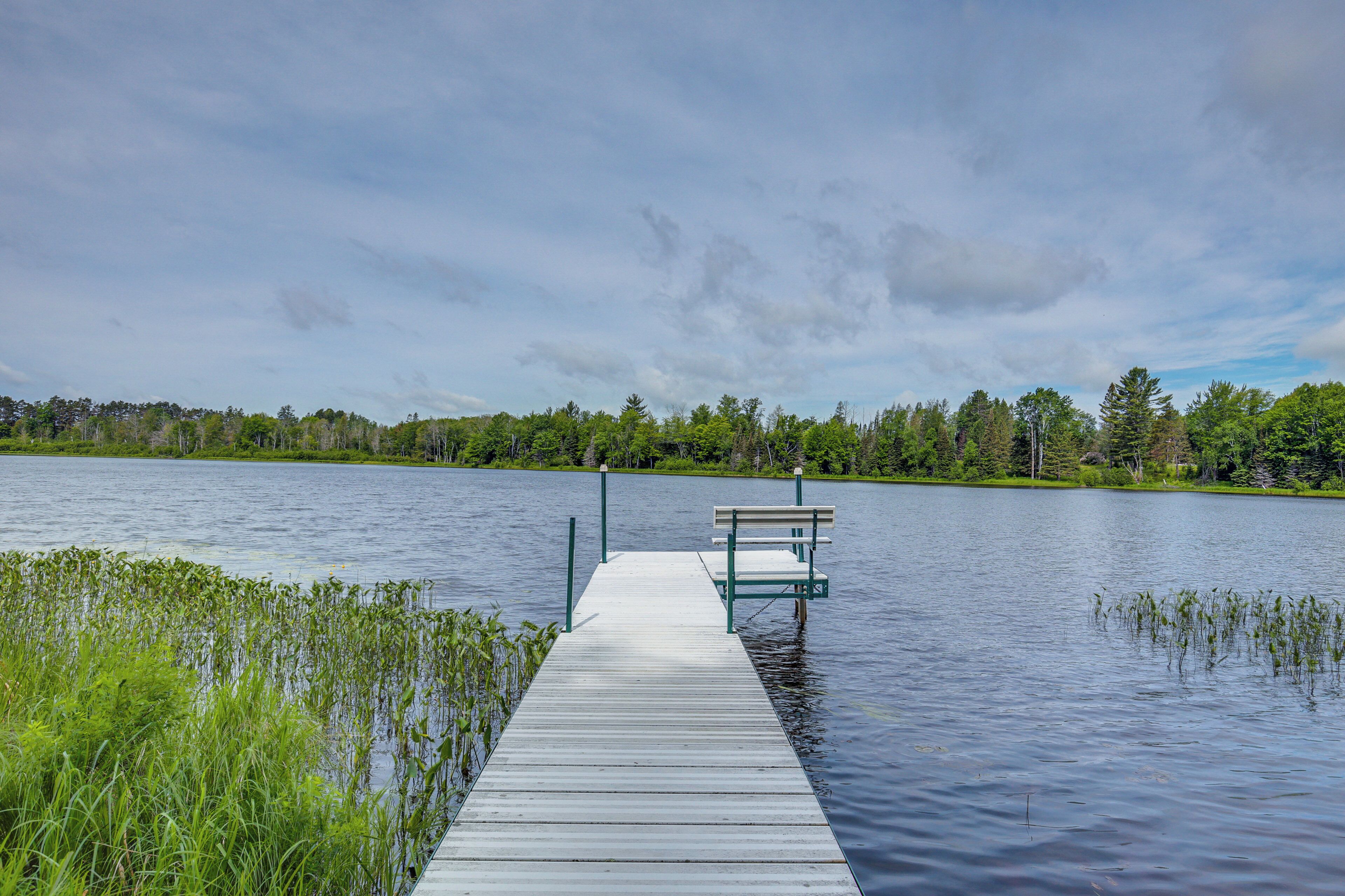 A wooden pier extending into a calm lake, surrounded by lush greenery and trees.