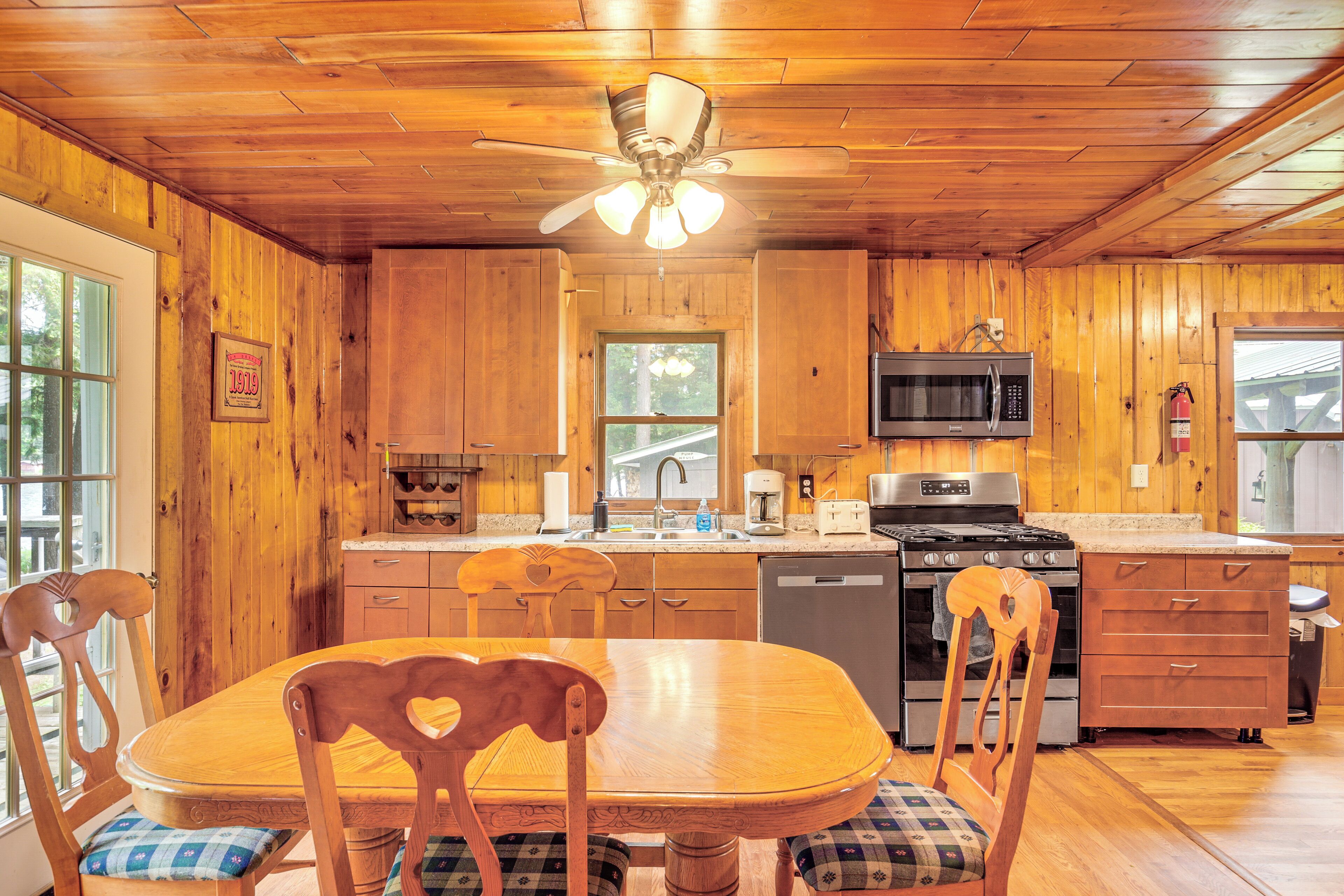 L’intérieur d’un chalet en bois comprend une table à manger, des chaises, un ventilateur de plafond, une cuisine équipée et des murs en bois.