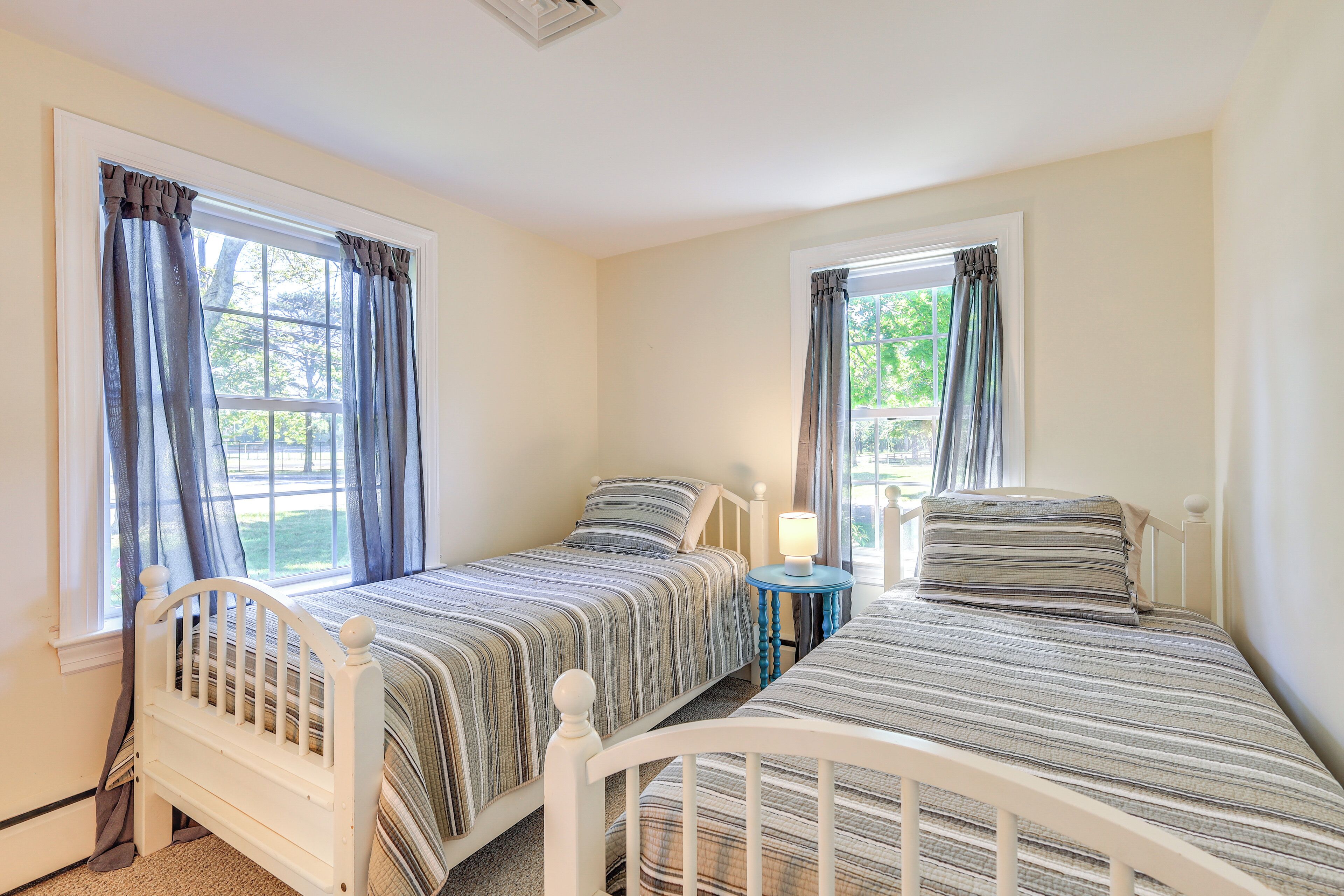 A bedroom with two single beds, a nightstand with a lamp, and a window with curtains.