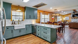 A modern kitchen with wooden cabinets, a central island, and a dining area with a fireplace.