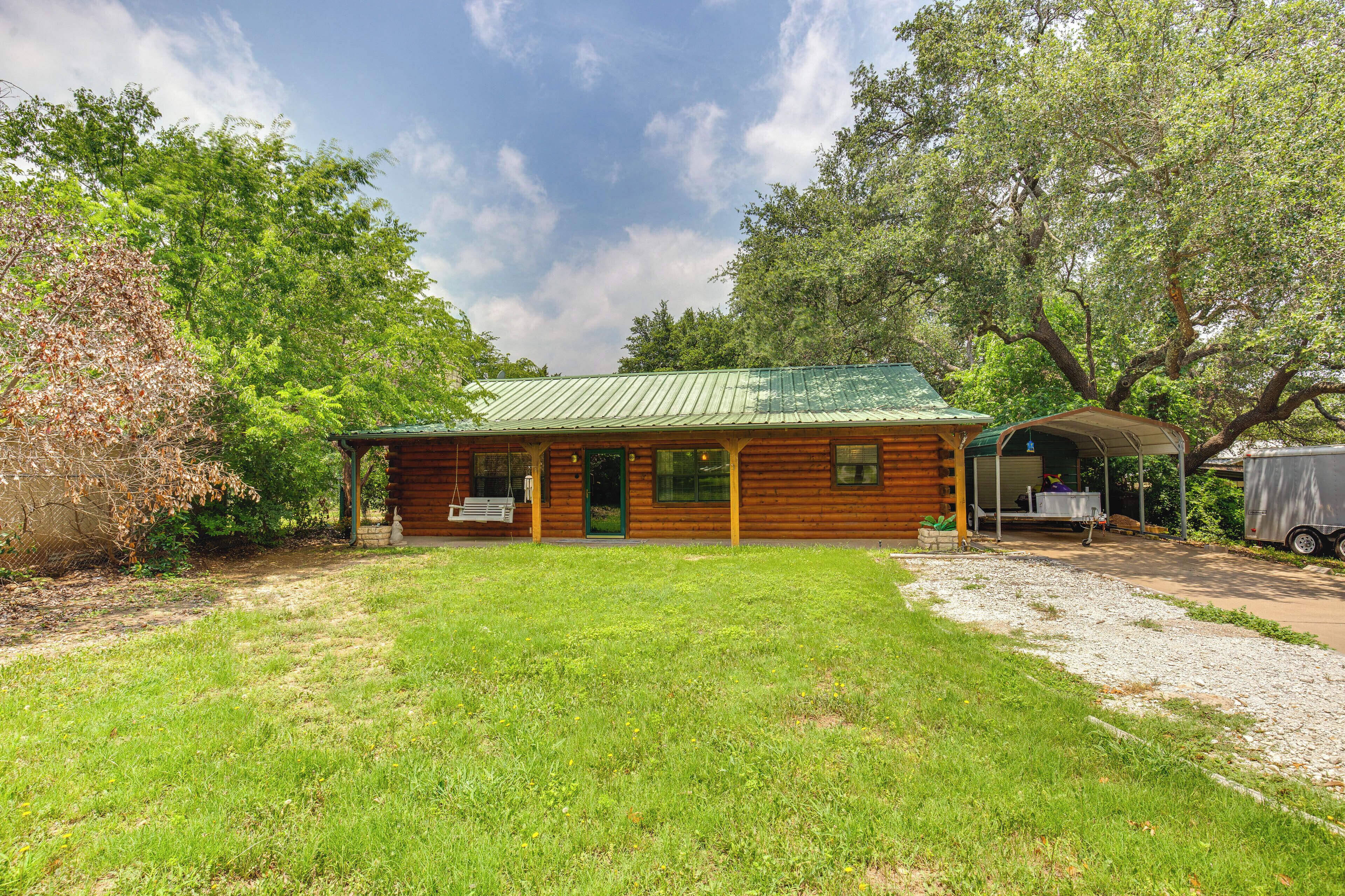A rustic log cabin with a green metal roof, a porch, and a covered outdoor seating area.