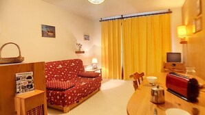 Ein gemütliches Wohnzimmer mit einem rot gemusterten Sofa, einem Holztisch mit einer Toastmaschine, einer Lampe und einem Fernseher.