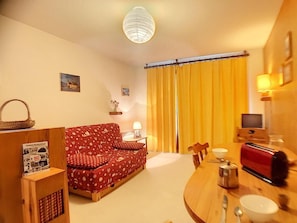 A cozy living room with a red patterned sofa, a wooden coffee table with a toaster, a lamp, and a television.
