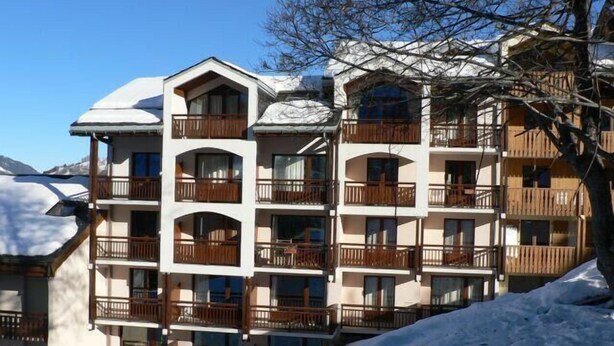 Ein mehrstöckiges Hotel mit Balkonen, einem schneebedeckten Dach und einer Bergkulisse.