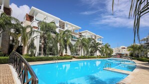 Una piscina con barandilla metálica, rodeada de palmeras y edificios modernos.