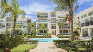 Un hotel moderno con varios pisos, piscina y jardines bien cuidados.