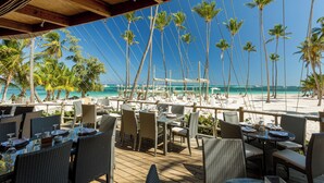 An outdoor dining area with wicker furniture and a view of the beach and ocean. - Paseo Del Mar B3ALO_200Mbps_Pool_Walk to Beach & Dining! (Bavaro-Punta Cana)