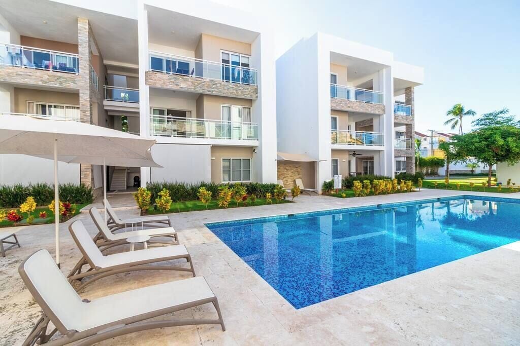 A modern hotel with a swimming pool, lounge chairs, and a landscaped garden.