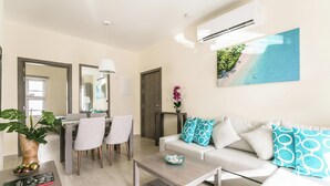 A modern living room with a sofa, coffee table, dining area, and a large window. - Paseo Del Mar B3ALO_200Mbps_Pool_Walk to Beach & Dining! (Bavaro-Punta Cana)