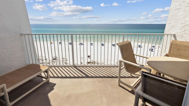 Ein Balkon mit Blick auf einen Strand, einem Tisch und zwei Stühlen.