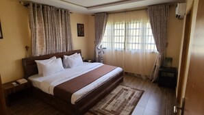 Een slaapkamer met een groot bed, gordijnen, een nachtkastje en een raam met gordijnen, plus een wandairconditioner.