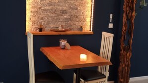 Un comedor con mesa y sillas de madera, pared de ladrillo con iluminación decorativa y una planta ornamental.