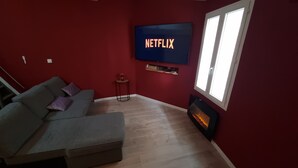 Una sala de estar con un sofá seccional gris, un televisor de pantalla plana montado en la pared, una mesita auxiliar y una chimenea.