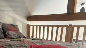 Una camera da letto con una testiera in legno, un letto con copripiumino grigio e decorato, e un pavimento in legno.