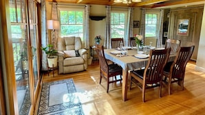 A dining area with a wooden table set for four, surrounded by chairs, with a view of greenery outside. - Best Views-Next to RMNP-Hike from House-HotTub-Fireplace-Coaster Passes-King Bed (Estes Park)