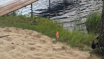 Ein sandiger Strand mit einer hölzernen Mole, die sich in ruhiges Wasser erstreckt.