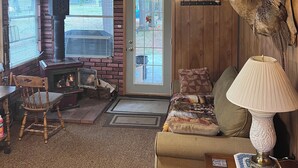 L’intérieur chaleureux d’un chalet avec un plafond en bois, une cheminée, un canapé, une lampe et une tête de cerf accrochée au mur.