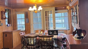 Un intérieur en bois avec une table de salle à manger ronde, des chaises, un lustre et un buffet orné d’une décoration représentant un oiseau.