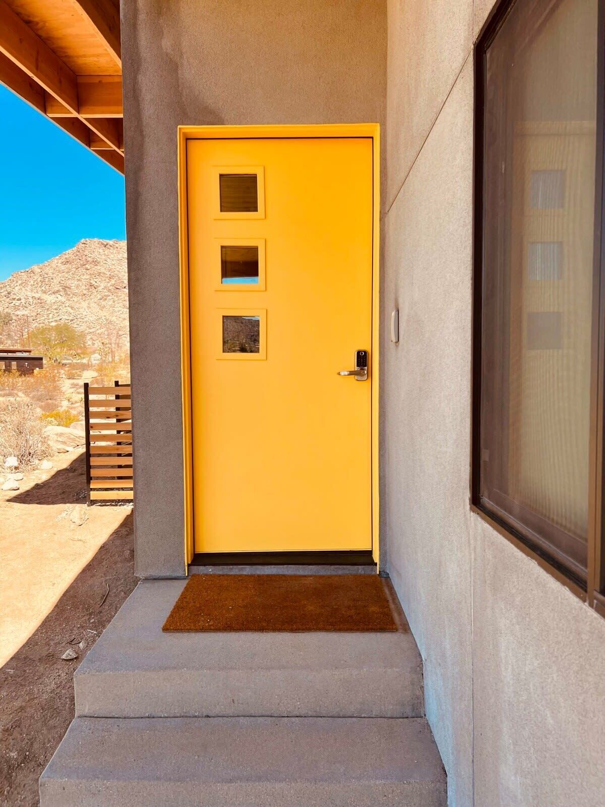A yellow door with a small window, a doorbell, and a doormat.