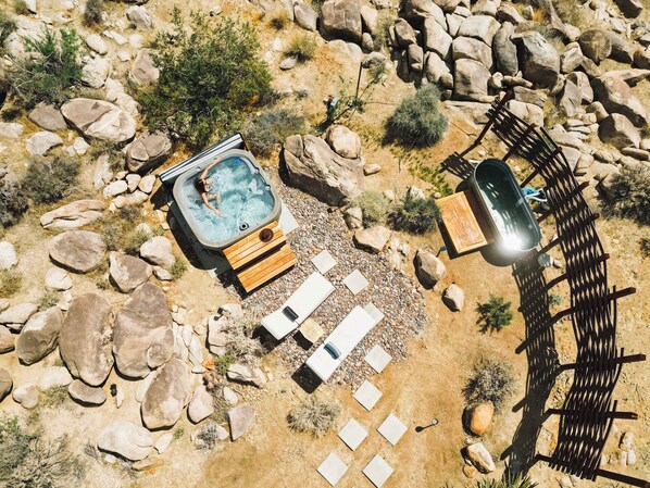 An outdoor hot tub surrounded by rocks and a wooden deck with lounge chairs. - Orion Minor By Homestead Modern (Joshua Tree)