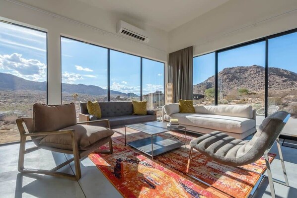 A modern living room with large windows, a sofa, a chair, and a coffee table.