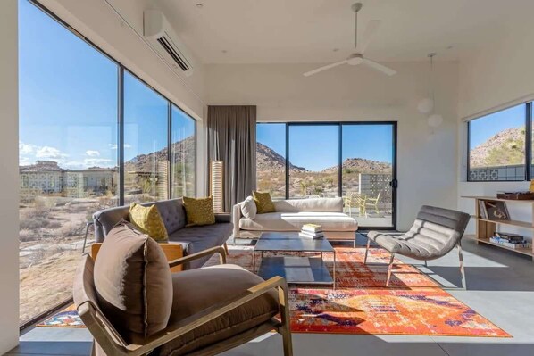 A modern living room with large windows, a sofa, a coffee table, and a chair.
