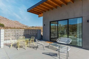 A modern outdoor patio with a wooden ceiling, a glass wall, and a seating area with metal chairs.