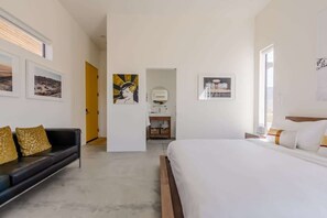 A modern hotel room with a bed, a sofa, and artwork on the walls.