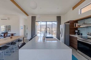 A modern kitchen with a central island, a dining area with a long table and chairs, and a view of mountains through large windows.