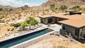 A desert landscape with a modern house featuring a swimming pool, lounge chairs, and a mountain in the background. - Orion Major By Homestead Modern (Joshua Tree)