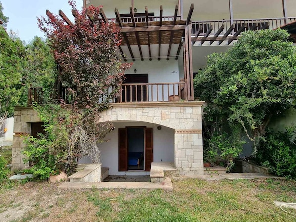 A two-story building with a stone archway entrance, a balcony with wooden railings, and surrounding greenery.