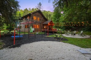 A wooden cabin with a playground, outdoor seating, and string lights.