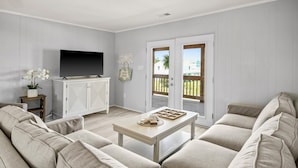 A living room with a beige sofa, a coffee table, a TV, and a sliding glass door leading to an outdoor area. - Inlet Paradise A - Your Perfect Coastal Escape! (Murrells Inlet)