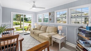 A room with a beige sofa, a wooden dining table, a white nightstand, and a bookshelf. - Inlet Paradise B Beautiful Condo Walking Distance to Beach! (Murrells Inlet)