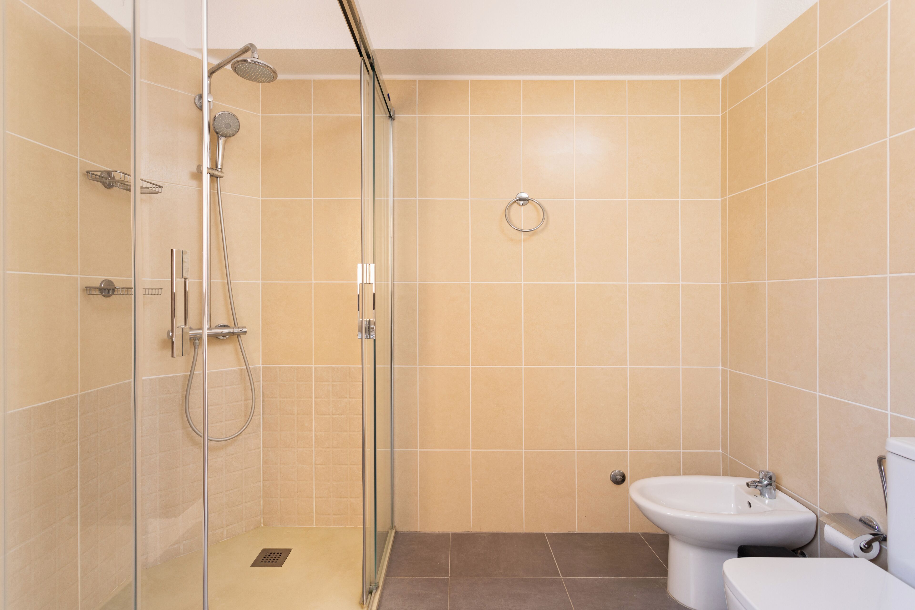 Een moderne badkamer met een douche met glazen wand, een hygiëneschuiver en een toilet.