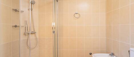 Een moderne badkamer met een douche met glazen wand, een hygiëneschuiver en een toilet.