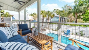 A covered outdoor area with a pool, seating, and a view of the neighborhood. - Uncloudy Day hosts 10 guests with a Pool (St Simons Island)
