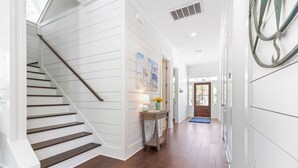A hallway with white paneled walls, a wooden staircase, and a door at the end. - Uncloudy Day hosts 10 guests with a Pool (St Simons Island)