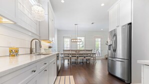A modern kitchen with white cabinetry, a stainless steel refrigerator, and a dining area with a wooden table and chairs. - Uncloudy Day hosts 10 guests with a Pool (St Simons Island)