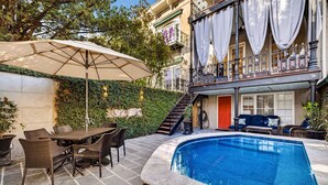 Zona de piscina con mesa y sillas, una sombrilla y una escalera que lleva a un nivel superior.