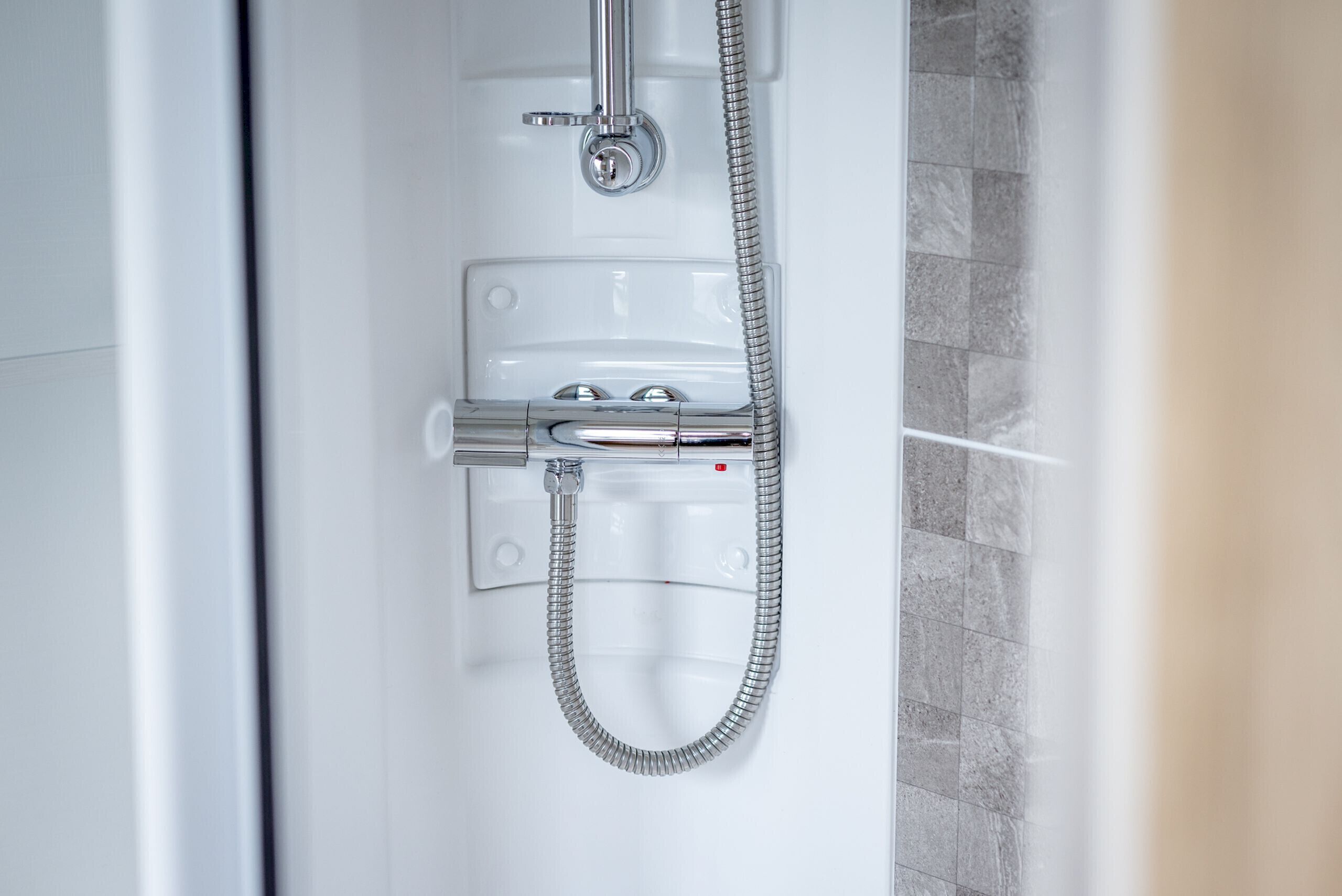 A modern shower with a flexible hose and a control panel.