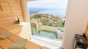 Una stanza in legno con un'ampia finestra vista su una cittadina e sull'acqua. Sono presenti panche di legno e una zona sauna.
