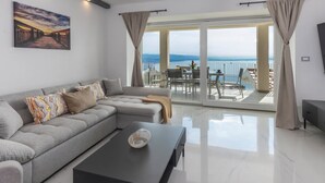 A modern living room with a grey sectional sofa, a black coffee table, and a large window with a view of the sea. - Apartments Bregha (Matulji)