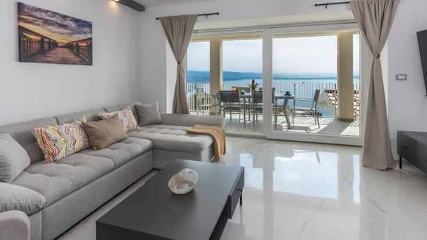 Un soggiorno moderno con un divano modulare grigio, un tavolino nero e una grande finestra vista mare.