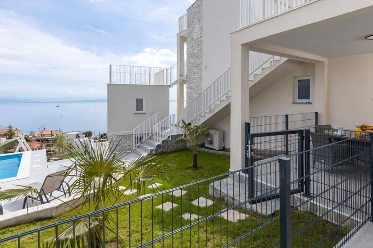A modern building with a pool, outdoor seating, and a view of the sea.