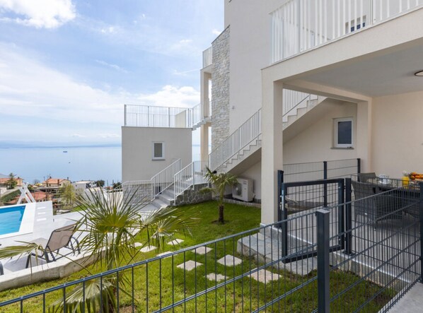 A modern building with a pool, outdoor seating, and a view of the sea. - Apartments Bregha (Matulji)