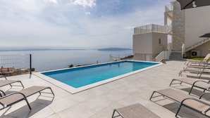 Una piscina con lettini, una scalinata in pietra e vista sul mare.