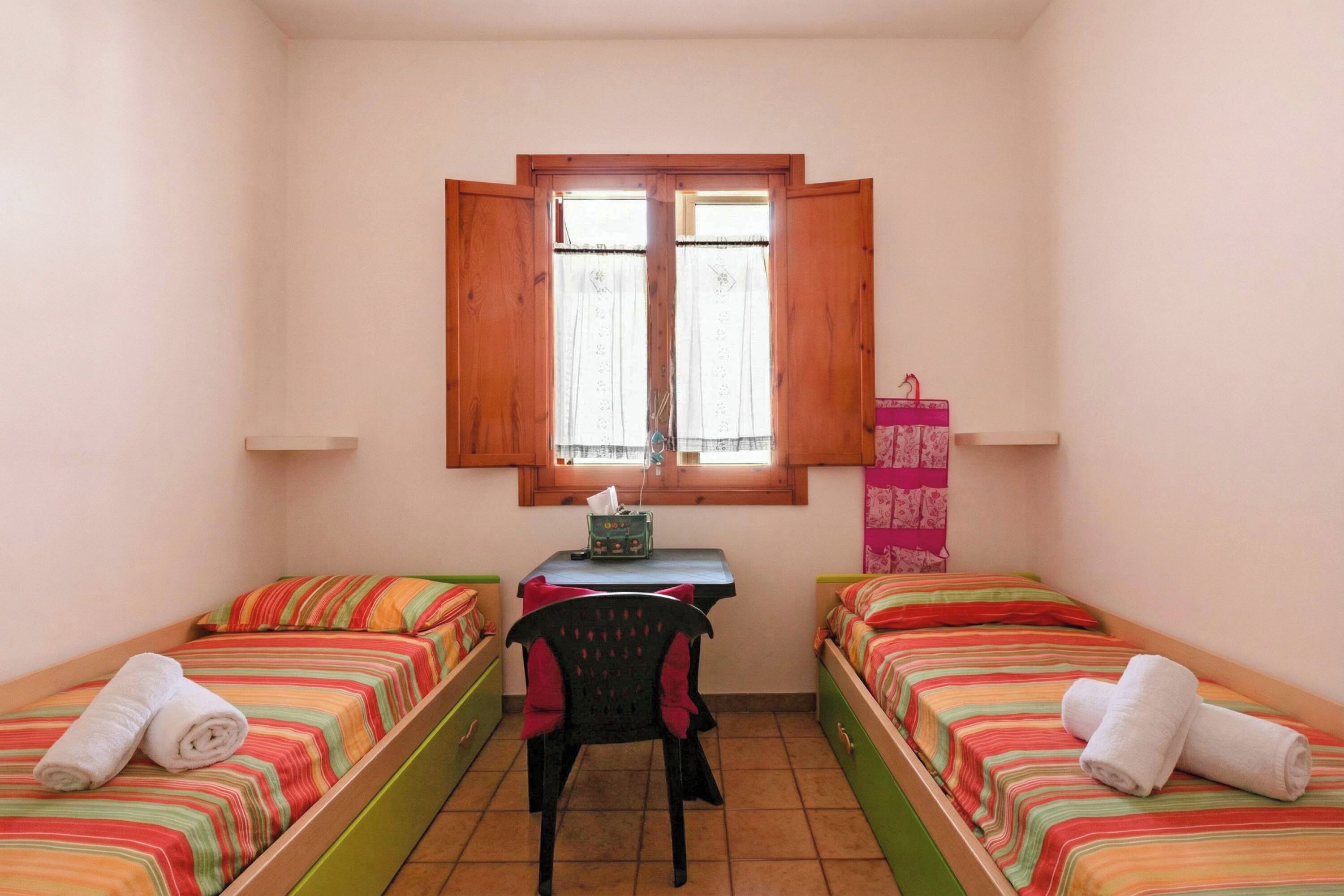 Ein kleines Zimmer mit zwei Einzelbetten, einem Schreibtisch, einem Stuhl und einem Fenster.