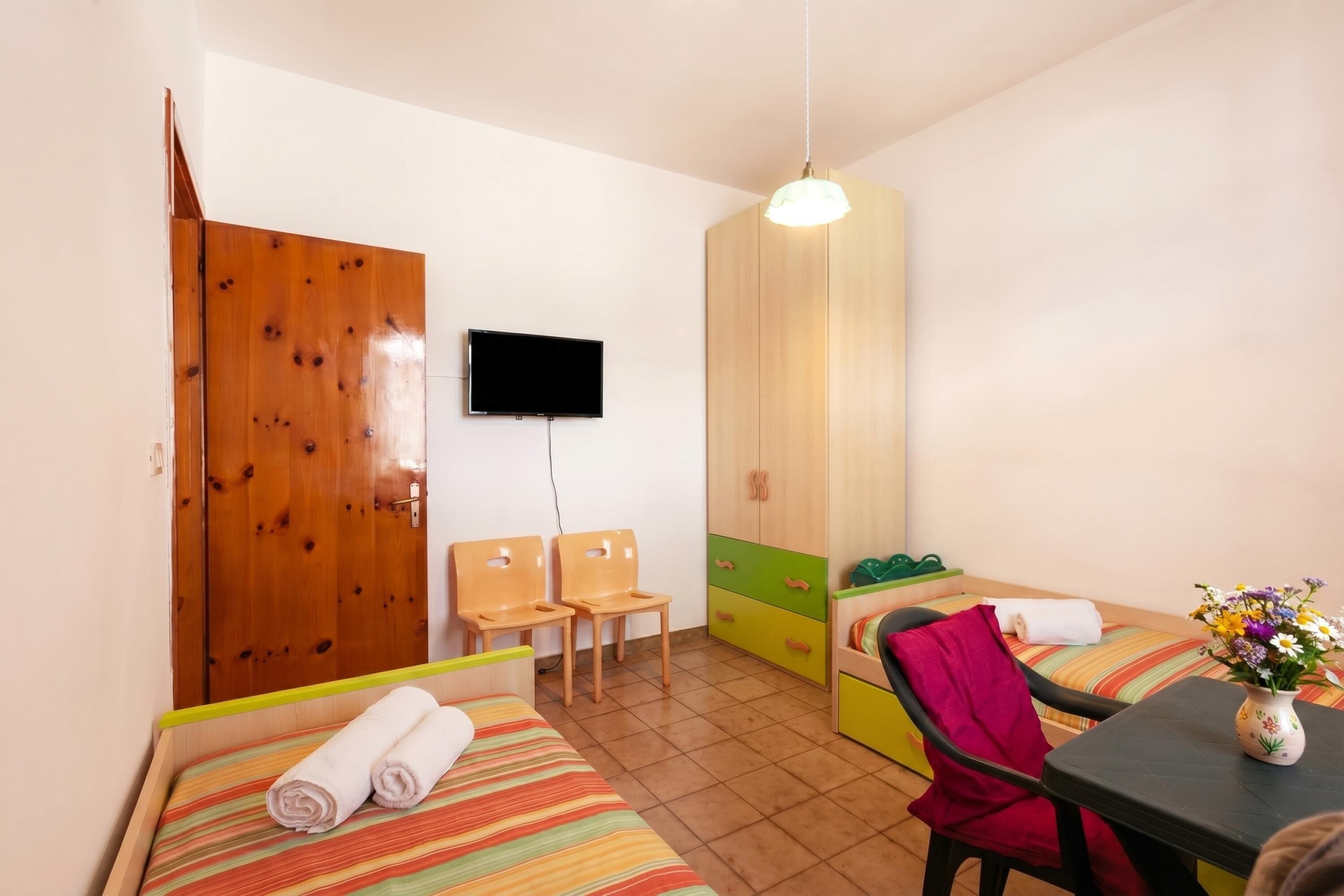 Ein Zimmer mit einem Bett, einem Sessel, einem Tisch, einem Fernseher und einem Kleiderschrank.